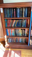 Bookshelf with multiple rows of vintage hardcover books with visible wear and varied colors of bindings.