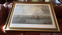Framed print showing full sea scene with multiple ships in Boston harbor and distant cityscape, placed on couch for size reference.
