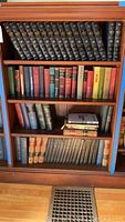 Bookshelf with various vintage hardcover books including Encyclopedia Americana multi-volume set on top shelf and assorted other books on lower shelves.