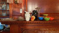 Wide view of all items including glass bowls, white pitchers, vases, turkey figurine, and colorful snack dishes on wooden mantle
