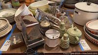 Photo of vintage kitchenware including toaster, salt and pepper shakers, baking dishes, ricers, mixing bowls, ceramic containers, and various pots showing condition and assortment of items.