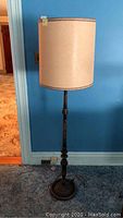 Front view of the floor lamp showing the full height, wooden base and beige fabric lampshade.