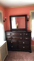 Full view of large dark wood dresser with attached matching mirror in room with peach walls and two wall sconces.