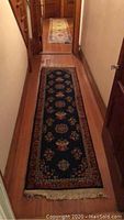 Front view of dark blue, red and gold patterned runner in hallway on wood floor, fringe visible