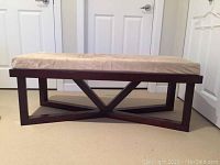 Full view of the bench showing the beige faux suede cushion and dark wooden geometric base.
