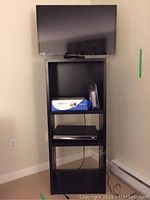 Full view of TV mounted above the black wooden shelving unit with items placed on shelves