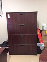 Front view of cherry laminate filing cabinet showing four stacked file drawers with black handles and locking mechanism on the top drawer.