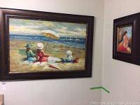 Large framed oil painting showing three figures on a beach under an umbrella with sailboats in the background.