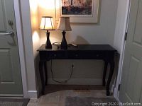 Full view of the black wooden console table with 3 drawers and 2 black table lamps on top, showing table design and arrangement.