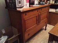 Full sideboard showing two drawers and two doors with brass hardware, placed against a wall with a box and other items nearby.