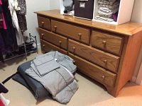 Photo showing full view of the solid oak dresser with seven drawers and king size bedding set folded and placed on the floor.