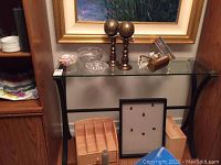 Full view of glass top console table with various decorative items on and below it including crystal ashtray, leaded bowl, wooden boxes, shadowbox frame, and two metallic orbs on stands