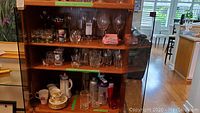 Wooden shelving with various glassware including beers mugs, shooter glasses, water bottles, and wine glasses. China on bottom shelf is excluded from sale.