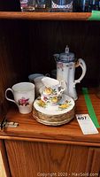 Shelf display of Royal Albert fine china pieces including teapot, teacups, saucers, and plates arranged on wooden shelf