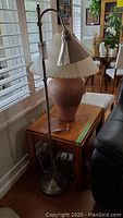 Tall floor lamp with metal shade next to wood end table with natural finish, showing scale and condition