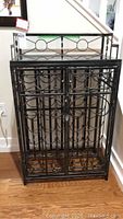 Full view of black metal wine rack with decorative front door and top shelf.