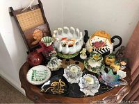 Various decorative items including porcelain teapot, candle holders, ceramic duck/goose bowl with a broken piece, art glass bowl and figurines on a wooden table.