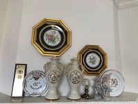 Photo showing full lot including two Limoges floral plates in gold and black octagonal frames, two white porcelain decorative vases with floral decoration, 50th and 60th anniversary plates, figurines, and a brass candle holder.
