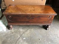 Front view of vintage wooden cedar chest showing carved front panel and claw-style feet.