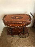 Full view of the vintage wooden drink cart with two drop leaves, positioned upright showing the floral inlay and wheels.