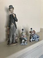 Front view of three Lladro porcelain figurines on display including Charlie Chaplin and two clowns.
