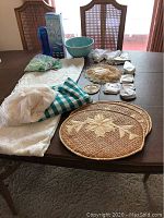 Overview of various linens, placemats, ceramic bowl, and other cloth items laid out on a dining table.