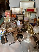 Photo showing assorted radios, lamps, picture frames, clocks, and decorative glassware arranged on a table.