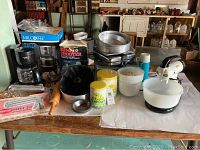 Photo of all kitchen items on a table including Sunbeam MixMaster, electric coffee maker, electric grill, waffle maker, cake pans, cookie cutters, cookie presses, rolling pin, and storage tins.