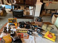 Wide view of entire lot showing cameras, binoculars, ViewMaster, multiple cases, and metal shelf.