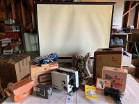 Full view of vintage movie equipment including projectors, cameras, accessories, and tripod screen in background