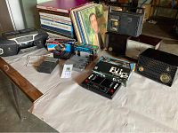 Wide view of lot including stack of LP records, portable cassette device, vintage radios, handheld Blip game, and cassette cases.