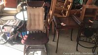 Photo showing antique dark wood rocking chair with cushioned beige back pillow and the dark wood antique side table with carved corner details.