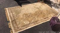 Full view of rectangular floral design area rug with beige and light brown tones, showing wear and fringed edges.