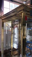 Full view of brass metal framed display cabinet with glass doors and mirrored back, showing overall design and structure.