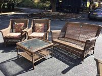 Wicker patio furniture set showing sofa, two chairs, and matching glass top coffee table outdoors.