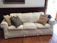 Front view of cream Thomasville sofa with six decorative pillows on wooden floor near a door.