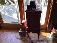 Wide view of large standalone wooden jewelry box with smaller boxes on top and beside it by a glass door with outdoor patio visible
