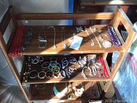 Front and slight top view of wooden shelving with costume jewelry including necklaces, bracelets, and brooches.