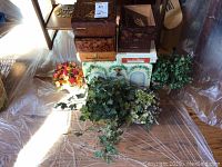 Photo showing four faux plants arranged among seven small storage boxes, including a Greensleeves hand-painted treasure chest.