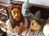 Photo showing three Wizard of Oz character cookie jars: Cowardly Lion, Tin Man, and Scarecrow on a table with other jewelry items in the background.