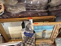 Photo showing large gold framed mirror behind framed painting of child on beach