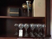 Shelf with 8 Neiman Marcus or Lenox stemmed wine glasses arranged in two rows; clear glass with subtle etched or painted details.