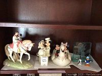 Wide shot of the Disney figurines collection on a wooden shelf including horse prince and princess, wedding couple Mickey and Minnie, swan boat Mickey and Minnie, Murano glass Donald Duck, Pluto, and signed Mickey figurine.
