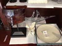 Lot items displayed on surface with 2 glass candle holders, Vannes Le Chatel crystal sculpture, white ceramic bird statue, Lenox Anniversary plate in box, brown decorative mask sculpture.