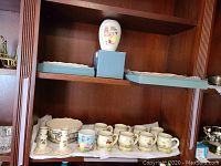 Full view of porcelain Snow White kitchenware and collectibles arranged on wood shelf, including multiple cups, candlestick holders, and bowls.