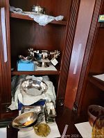 Silver plated and metal dishware displayed on shelves including bowls, rectangular butter dishes, an ashtray, and a decorative bowl.