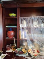 Shelf with multiple glass vases and bowls, some covered partially with plastic.