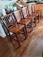 Five wooden bar chairs arranged in a row on a wooden floor, showing the overall appearance and condition.