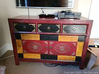 Front view of multi-color wooden TV cabinet with three drawers and two-door cabinet below, showing decorative painted designs and metal ring pulls.