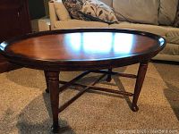 Oval chestnut stain coffee table with star inlay on the top surface, two levels of crossed rails connecting four legs, placed on carpeted floor in living room environment.